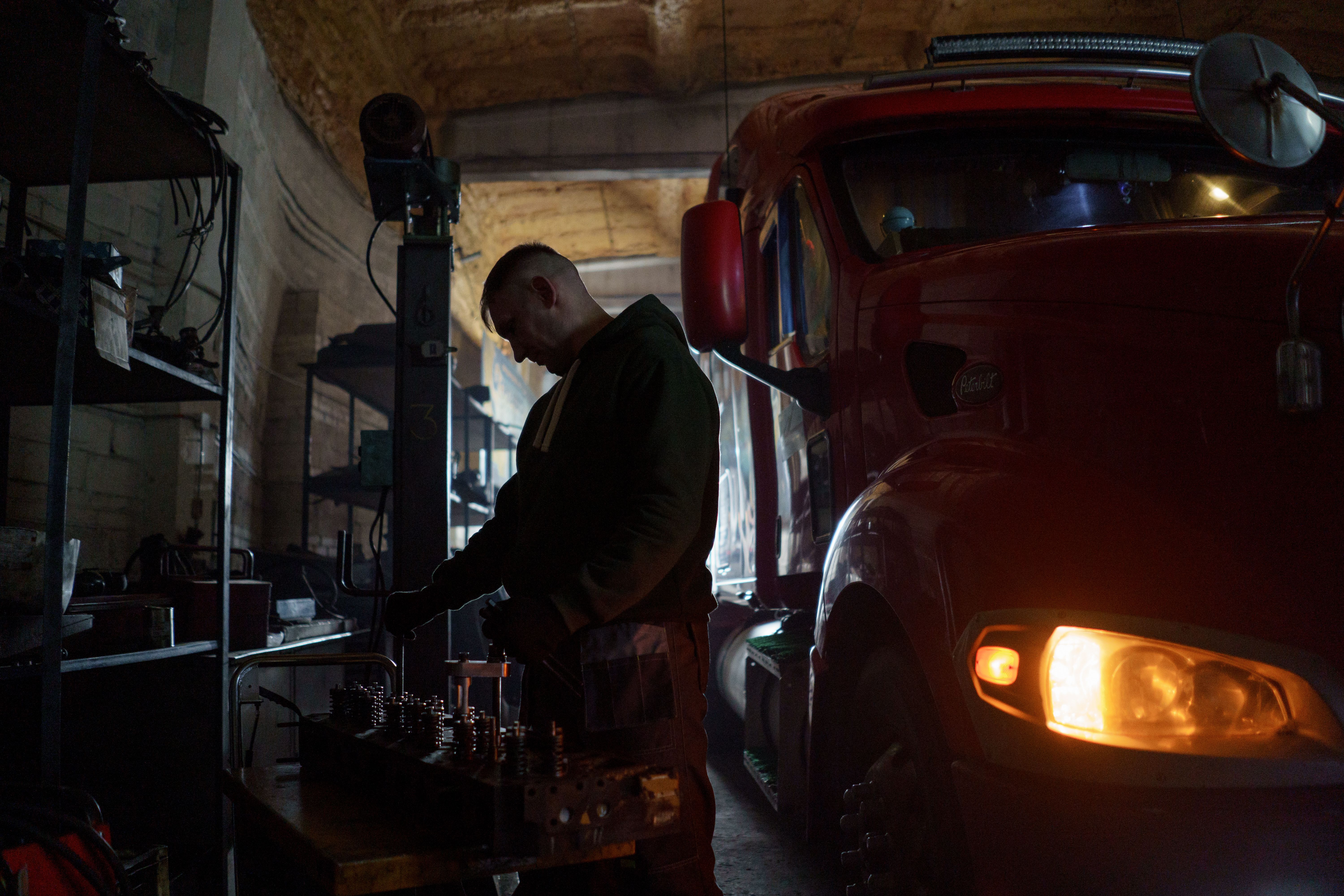 A mechanic focuses on his work beside a large red truck in a dimly lit workshop
