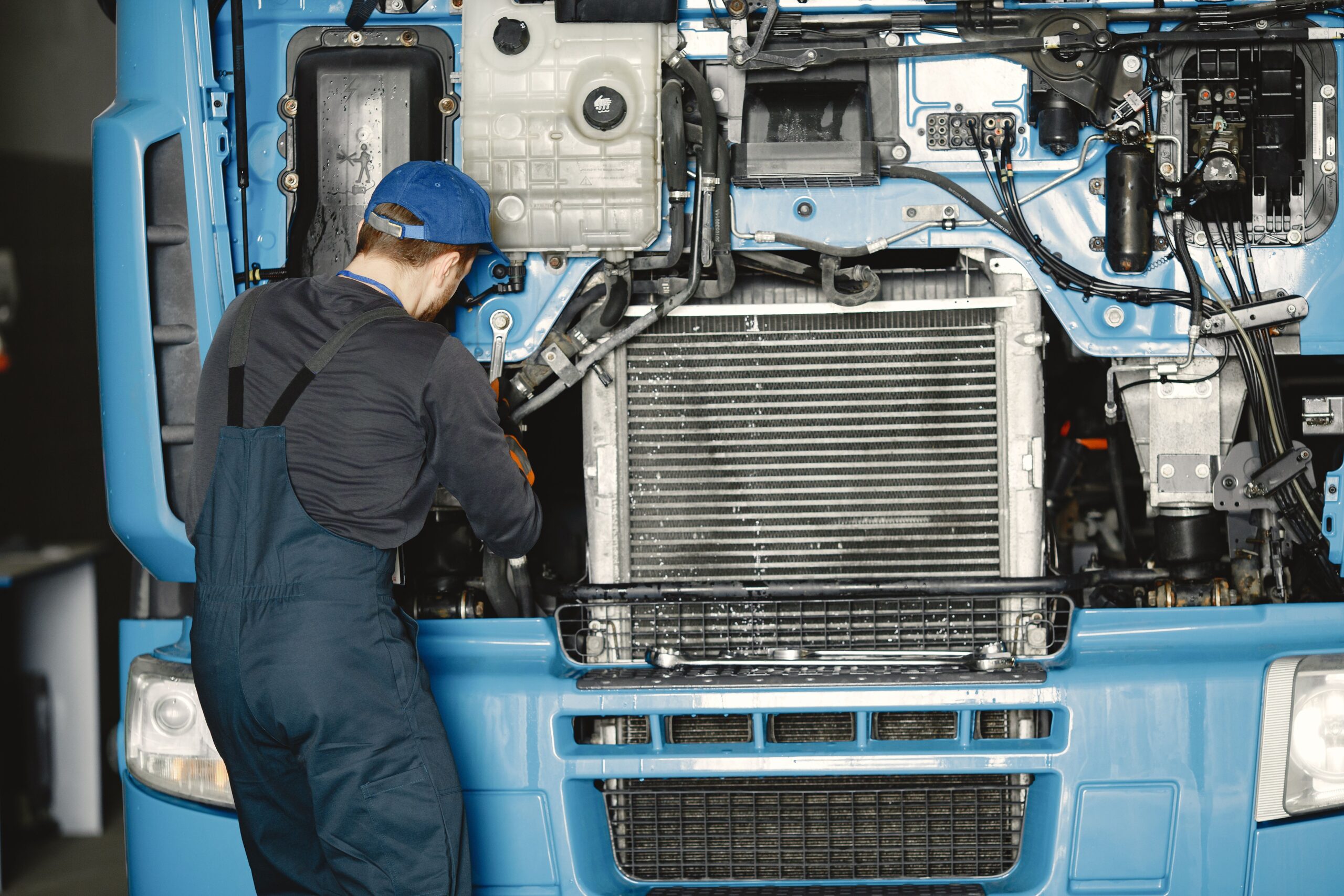 Mechanic in uniform working on a truck engine in an industrial workshop